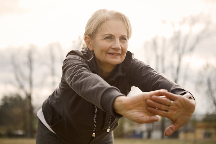 Woman in her 60s with blond hair  stretching her arms outside