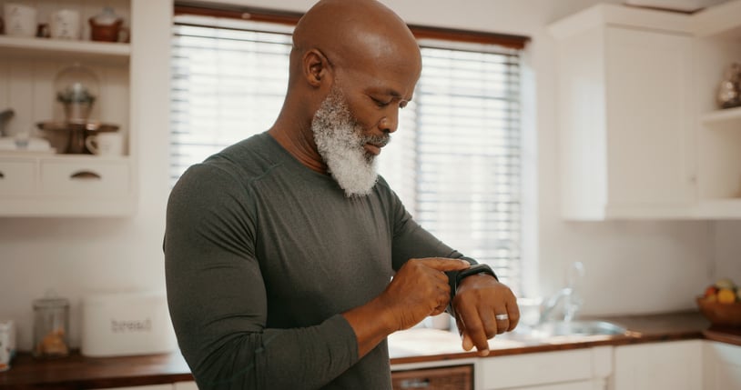 Bald black man looking at a fitness tracker on his wrist in a kitchen