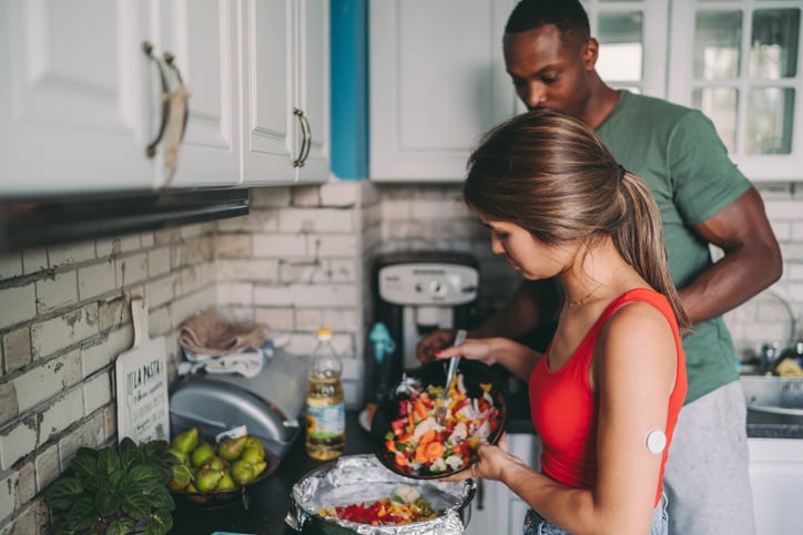 Woman wearing a continuous glucose monitor cooking with a man