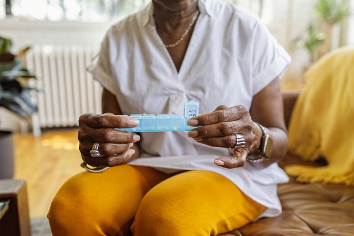 Senior black woman sits on couch with pill organizer