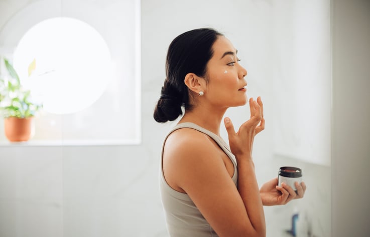 Woman applying sunscreen to her face in the bathroom