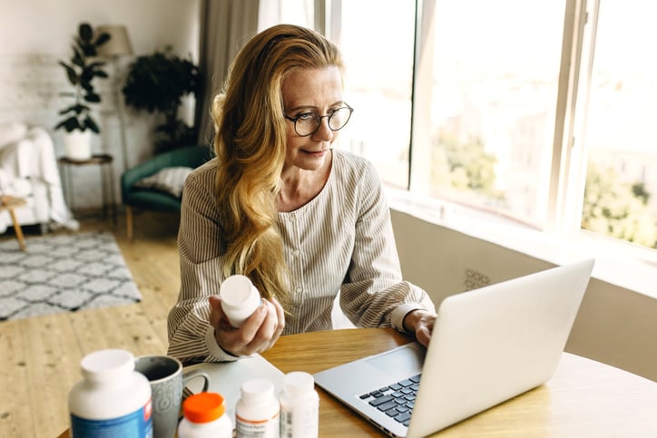 An older woman reading supplement bottles and looking them up online