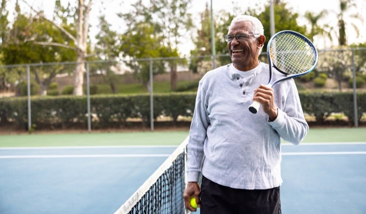 Senior black man holding a tennis racket and ball on an outdoor court