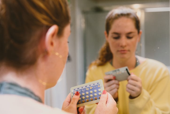 A woman's reflection in the mirror looking at birth control pills