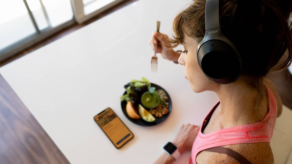 Woman wearing headphones eating lunch and looking at her phone