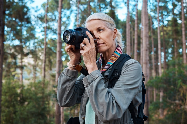 older woman with gray hair holding a camera in nature