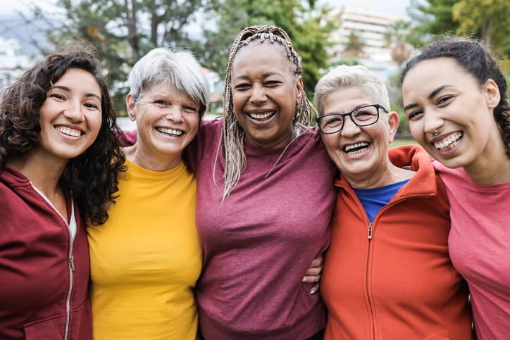 5 women of various ages and ethnicities with their arms around each other